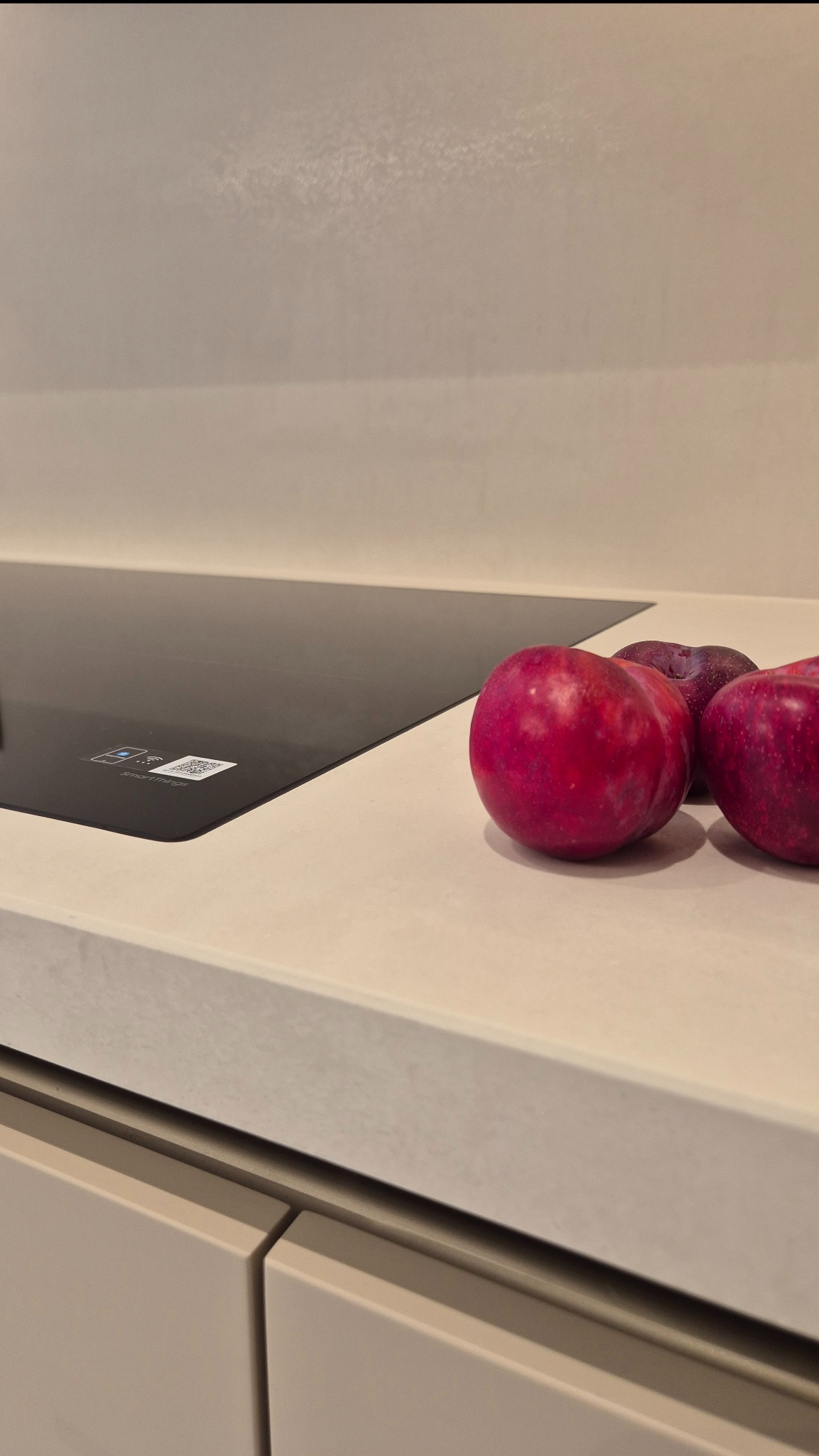 Płyta indukcyjna zlicowana z jasnym blatem kuchennym ze spieku, z owocami w tle. Minimalistyczna kuchnia, nowoczesny design.