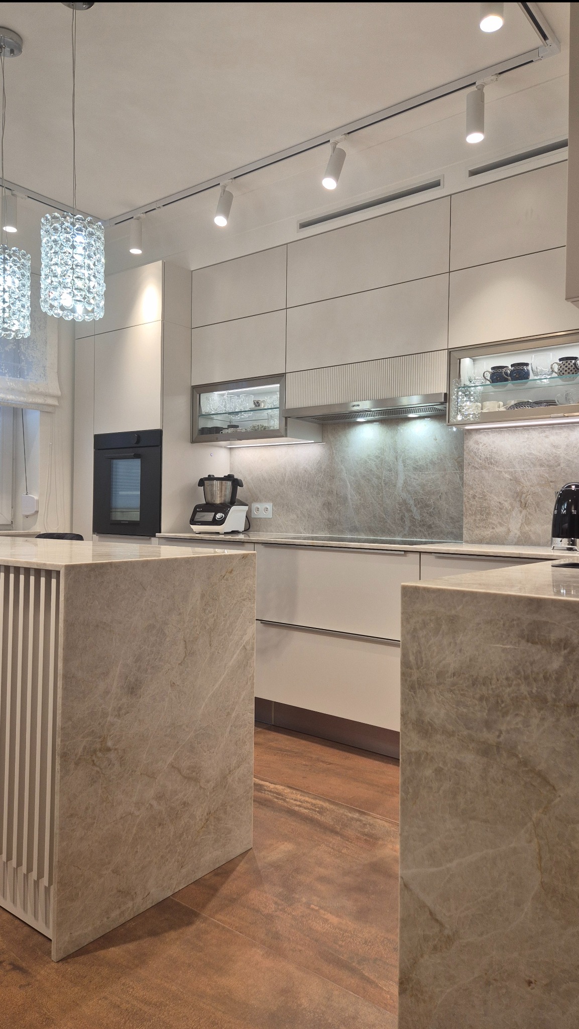 Elegancka kuchnia z wyspą i blatem z kwarcytu Taj Mahal. Ryflowane fronty wyspy, jasna zabudowa i oświetlenie punktowe tworzą spójną całość.