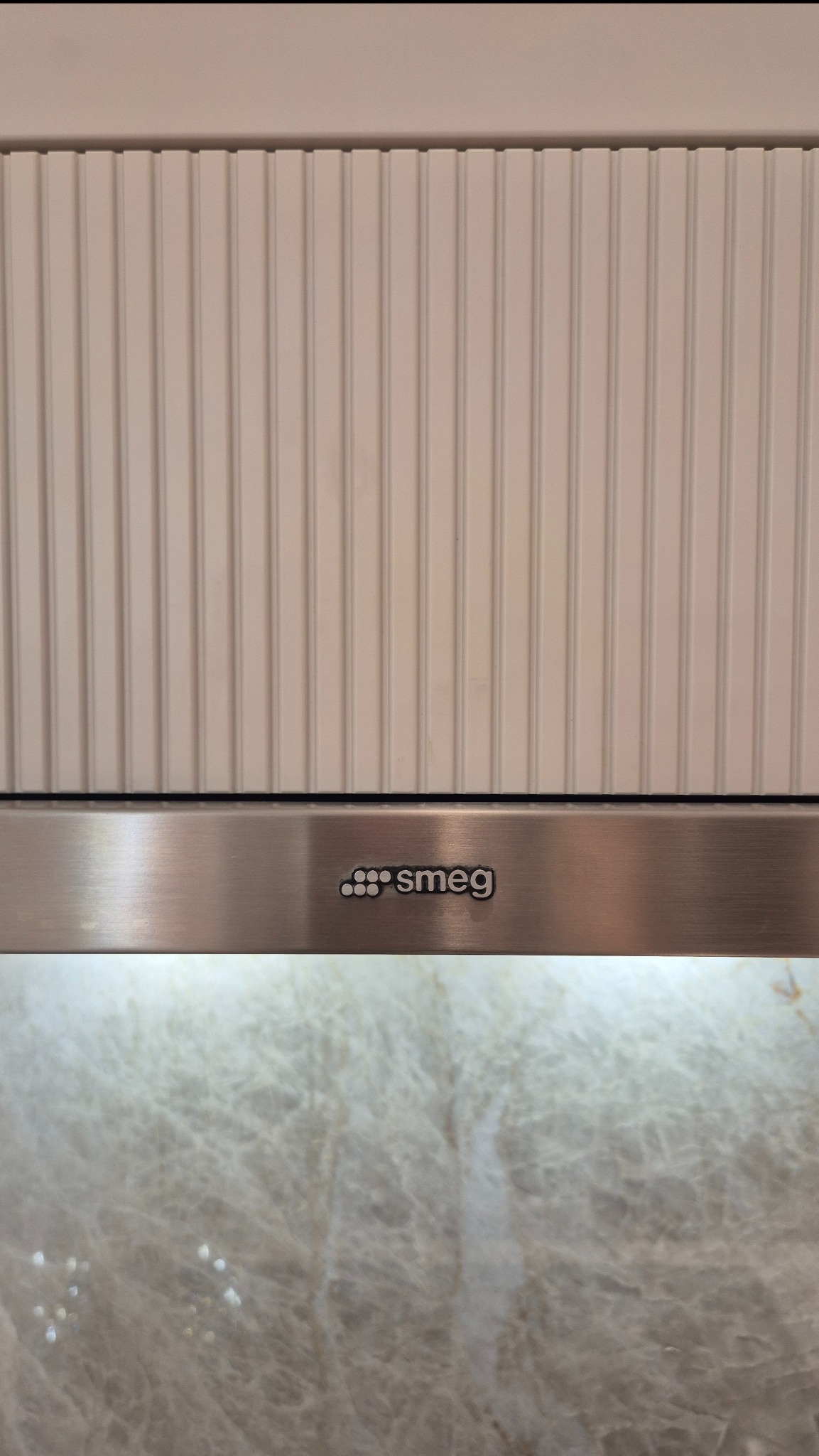 Detal ryflowanej szafki nad okapem Smeg, z blatem kamiennym w tle. Subtelna struktura i elegancki akcent w zabudowie kuchennej. Blat kamienny z wyraźnym wzorem.