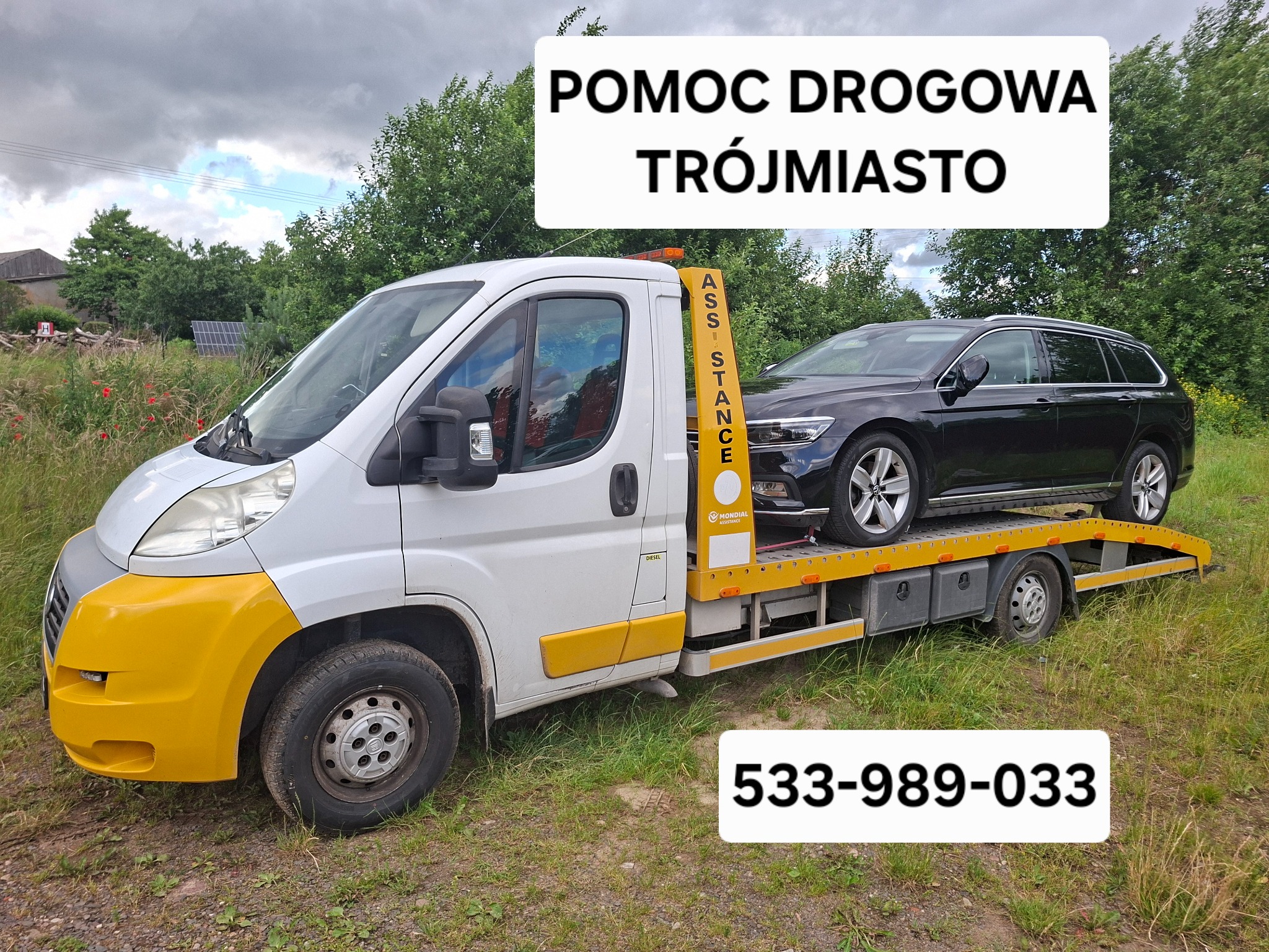 Laweta z czarnym samochodem osobowym na platformie, na tle zieleni. Na zdjęciu widoczny numer telefonu i napis Pomoc Drogowa Trójmiasto.