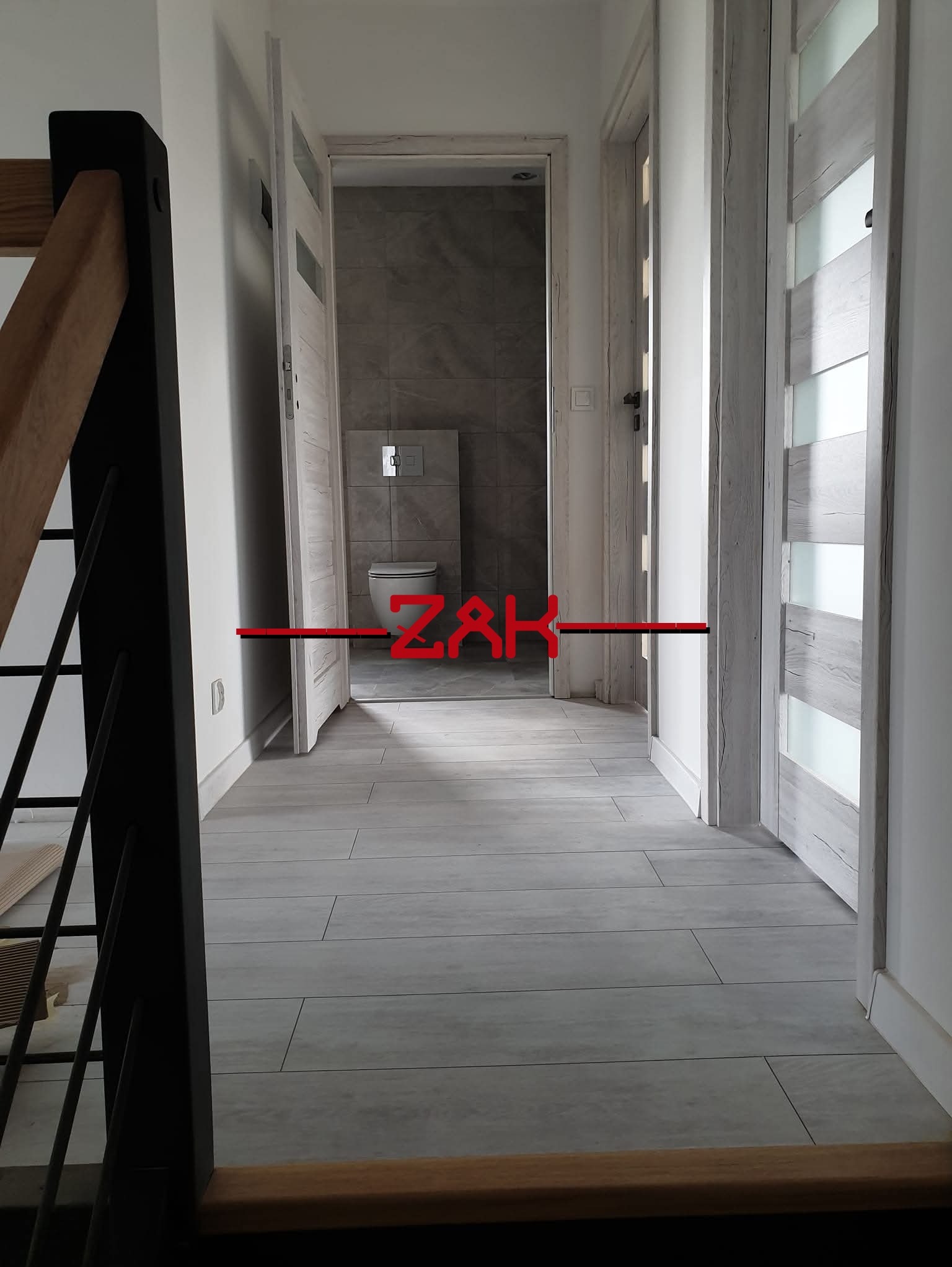 Korytarz po remoncie: jasne panele podłogowe imitujące drewno, białe ściany, dwoje drzwi wewnętrznych z przeszkleniami. Widok z góry schodów.