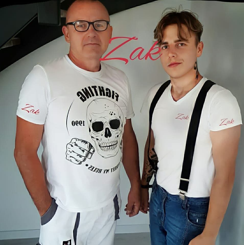 Portret dwóch mężczyzn w białych koszulkach z nadrukiem, prezentujących firmę ZAK. Jeden w okularach, drugi z szelkami i tatuażami. Jasne tło, naturalne światło.