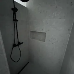 Nowoczesna kabina prysznicowa z czarną armaturą i wnęką w jasnych, kamiennych płytkach. Minimalistyczny design, ukończona realizacja.