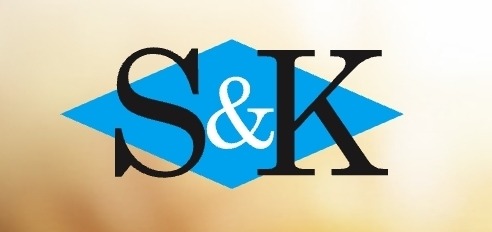 Logo 'S&K' w czcionce szeryfowej, czarne litery na błękitnym rombie, na rozmytym, ciepłym tle. Minimalistyczny design logo.