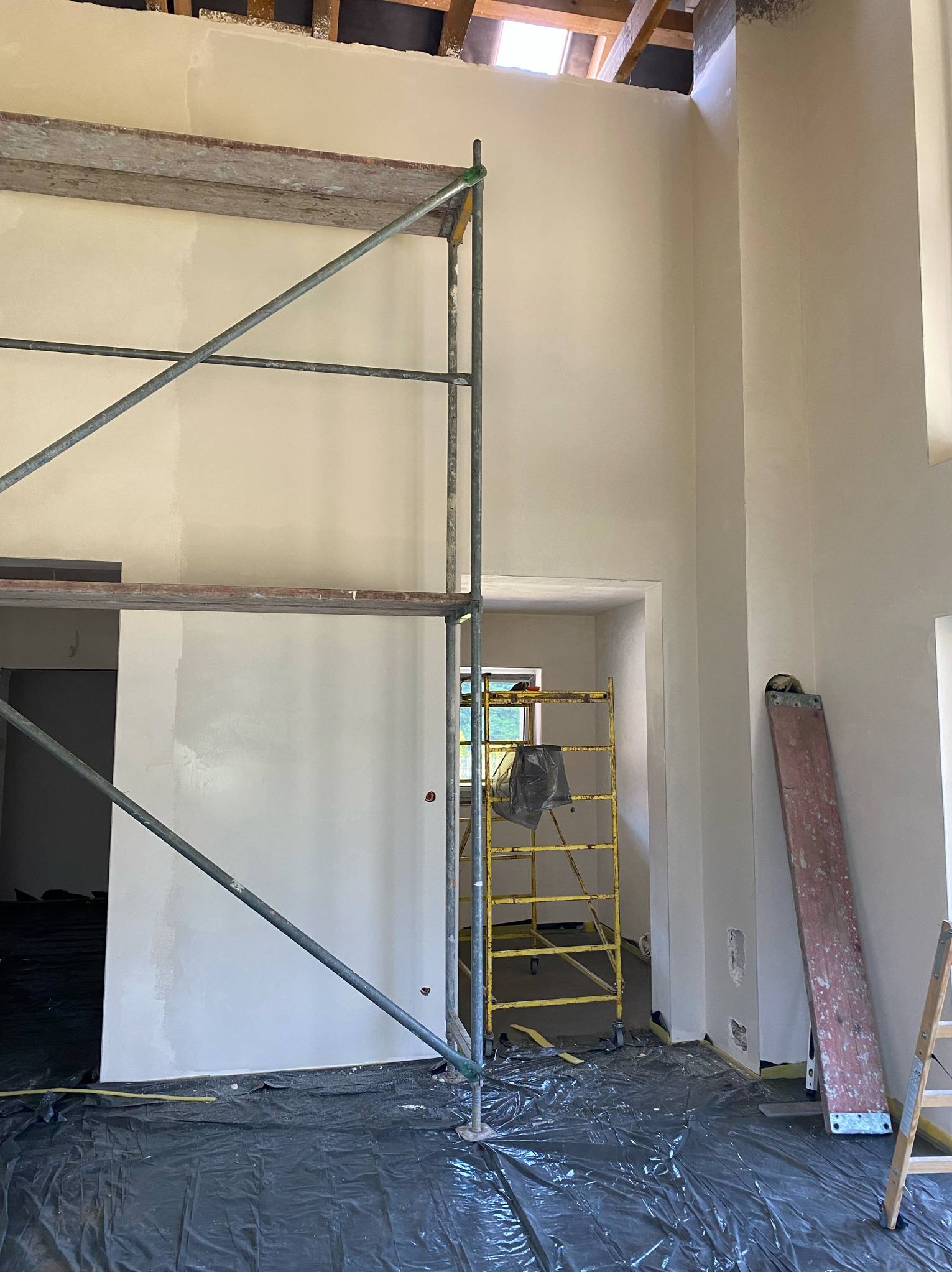 Wysokie wnętrze w trakcie prac wykończeniowych, z widocznym rusztowaniem i świeżo pomalowanymi ścianami w jasnym odcieniu, zabezpieczone folią ochronną na podłodze.