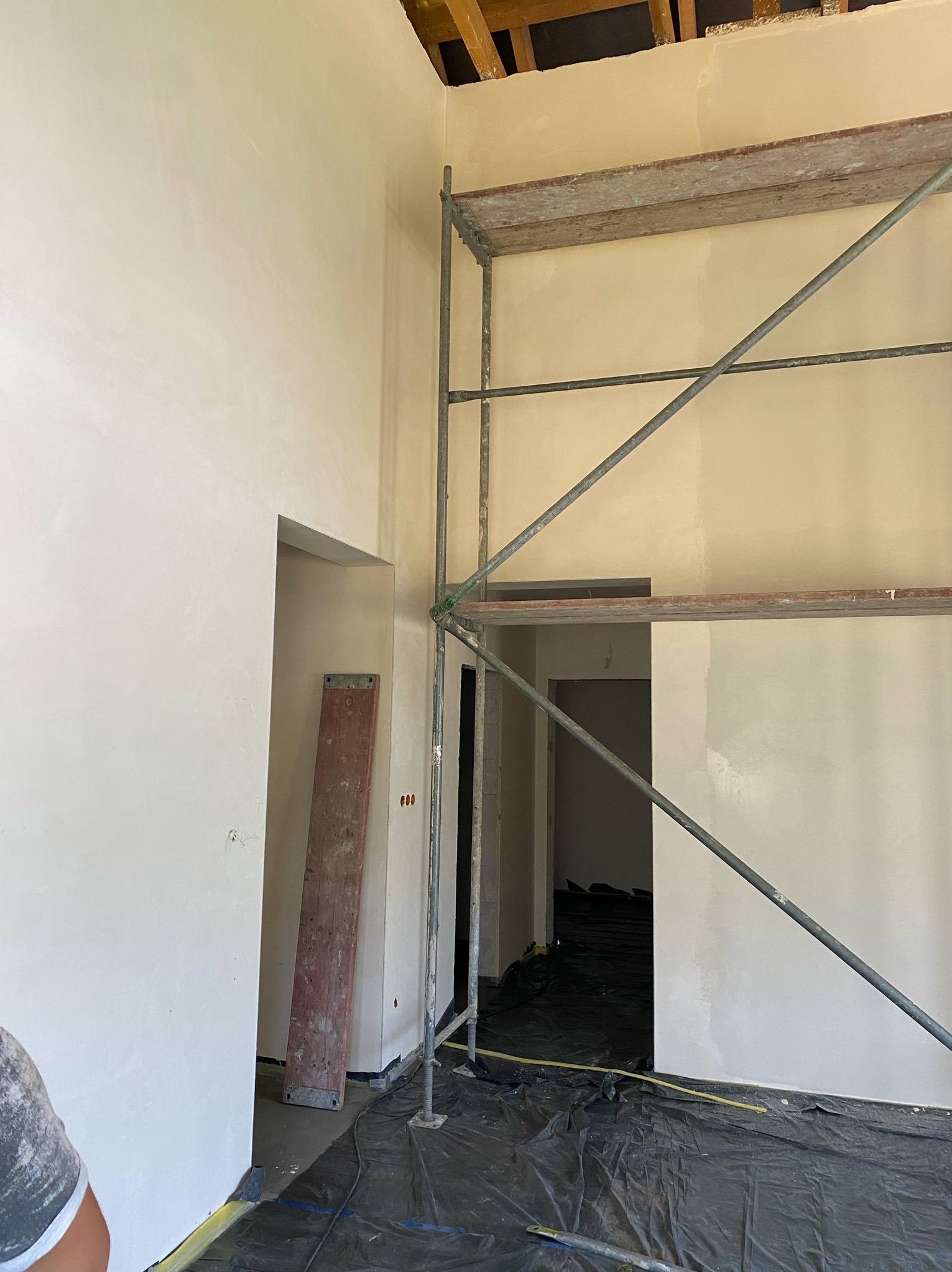 Wnętrze w trakcie prac wykończeniowych: ściany po szpachlowaniu, rusztowanie, podłoga zabezpieczona folią. Widoczne niedoskonałości, surowy stan.