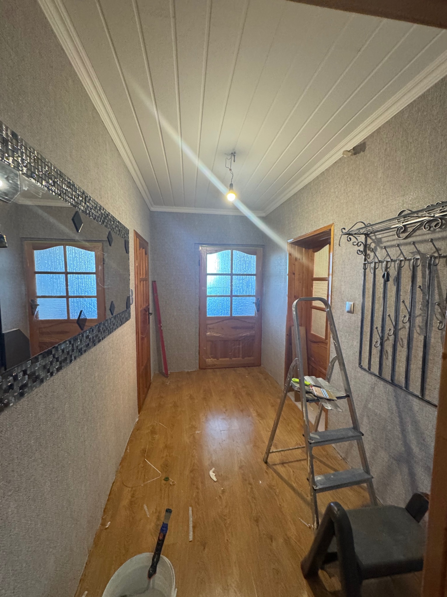 Korytarz w trakcie odświeżania: drabina, wiadro z farbą, ślady po remoncie na podłodze, lustro z mozaiką,  w tle drzwi z szybami.