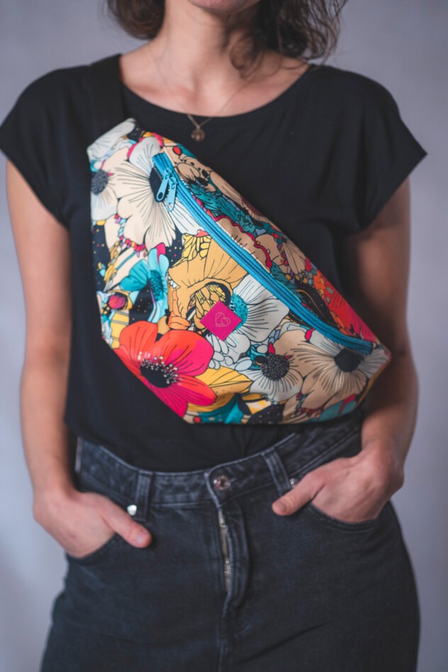 Kobieta prezentuje nerkę biodrową w kwiatowy wzór z turkusowym zamkiem, noszoną na skos przez ramię, w czarnym T-shircie i jeansach.