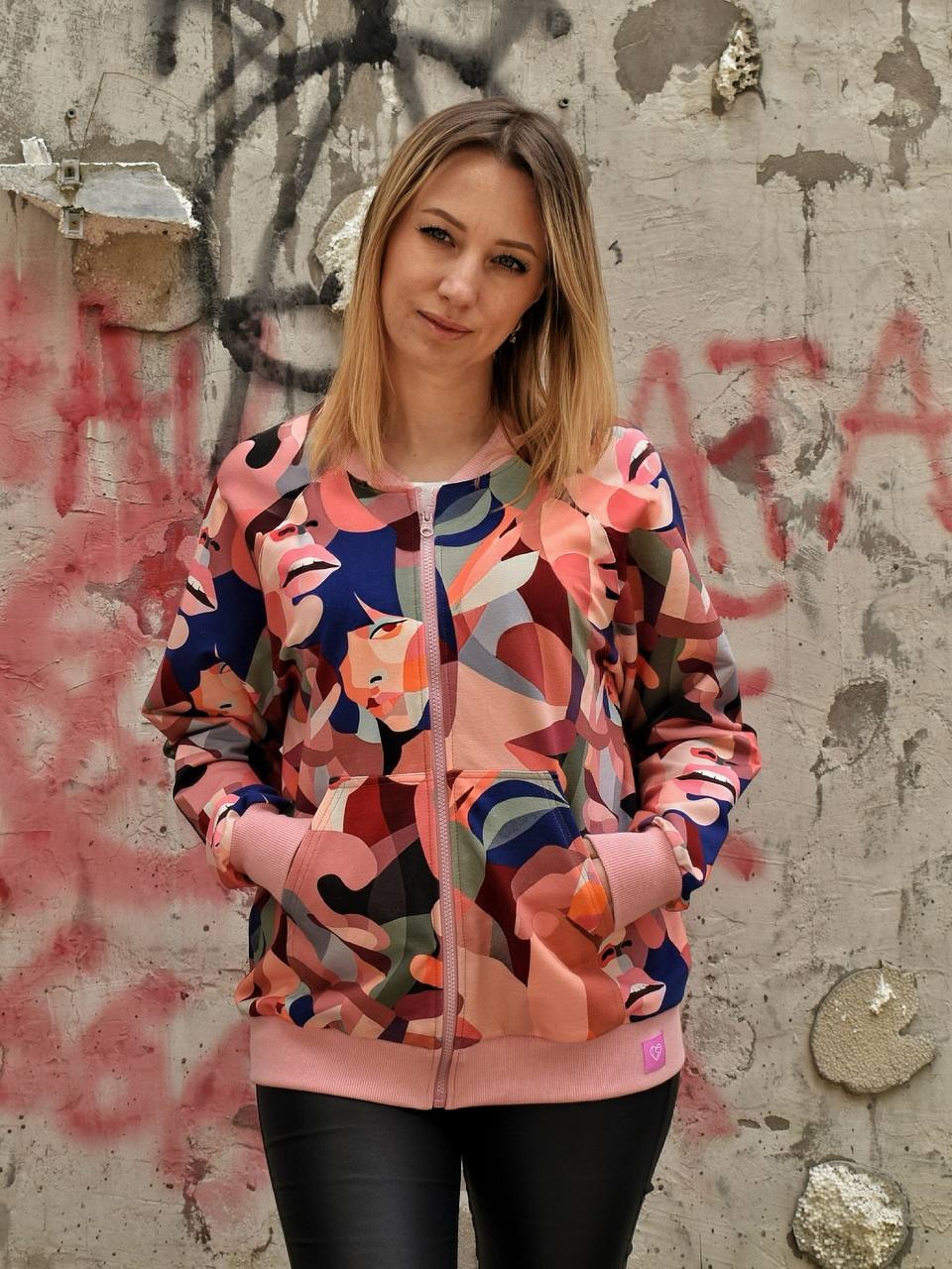 Kobieta w autorskiej bomberce z abstrakcyjnym wzorem na tle graffiti w Żywcu. Różowa lamówka i zamek. Prezentacja szytej na zamówienie odzieży.