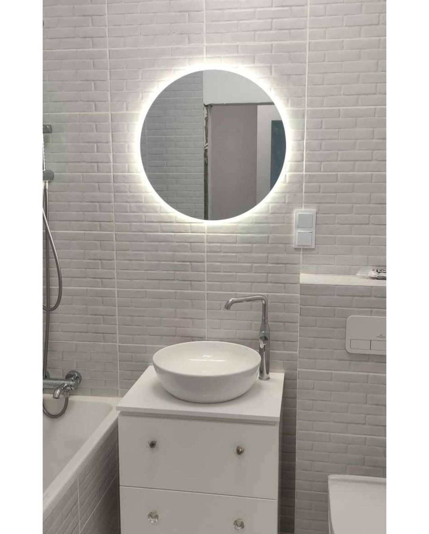 Biała łazienka po remoncie: umywalka nablatowa, bateria, okrągłe lustro z podświetleniem LED, płytki imitujące cegłę, armatura. Widok na fragment wanny i toalety.