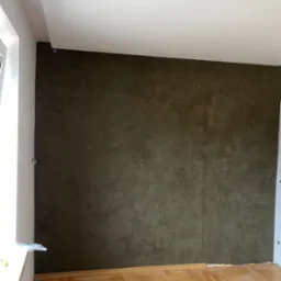 Ściana w odcieniach brązu z efektem dekoracyjnym, widoczna drewniana podłoga w jodełkę, fragment okna po lewej stronie.