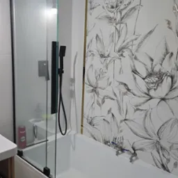 Nowoczesna łazienka z białą wanną, czarną armaturą i szklanym parawanem nawannowym. Ściana z motywem kwiatowym.