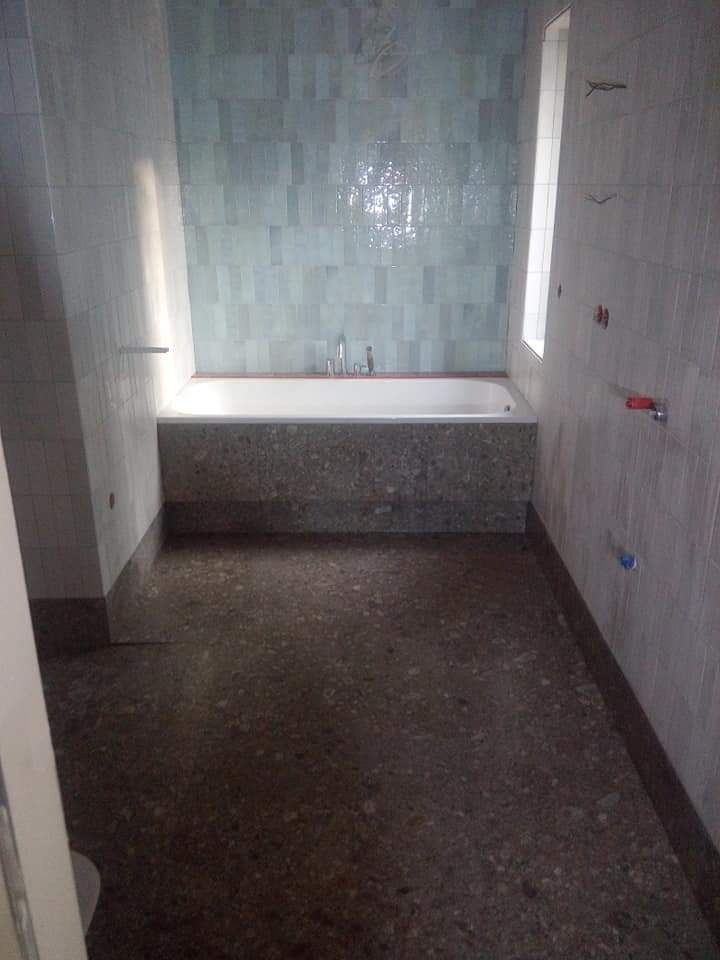 Wykończona łazienka z wanną obudowaną kamieniem i turkusowymi płytkami na ścianach. Widoczne instalacje wodne i posadzka z lastryko.