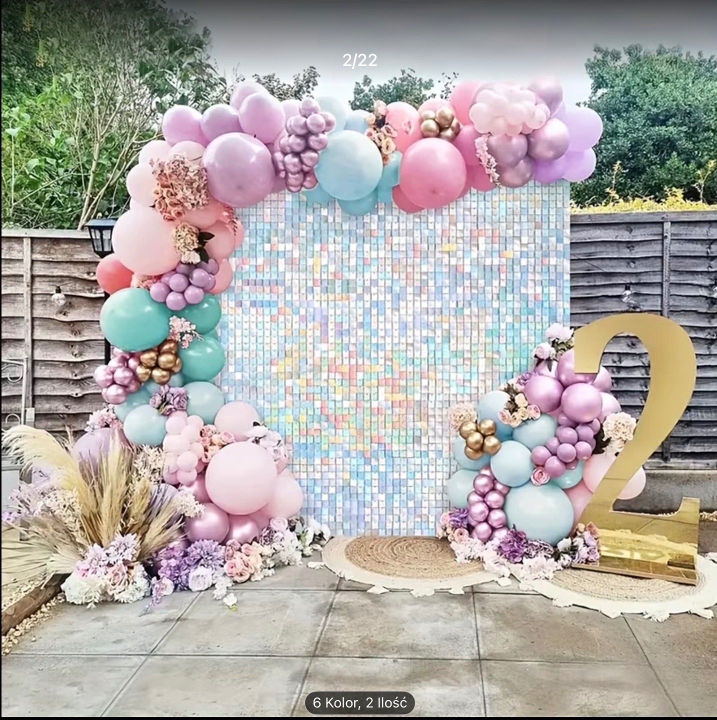 Pastelowa dekoracja urodzinowa z błyszczącym tłem, balonami, kwiatami i cyfrą '2' na zewnątrz, na tle drewnianego płotu.