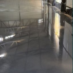 M-Bud Przemysłówka - Gładka, szara posadzka przemysłowa w hali, z widoczną konstrukcją stalową dachu i ścianami z blachy trapezowej. Światło dzienne wpada przez okna.