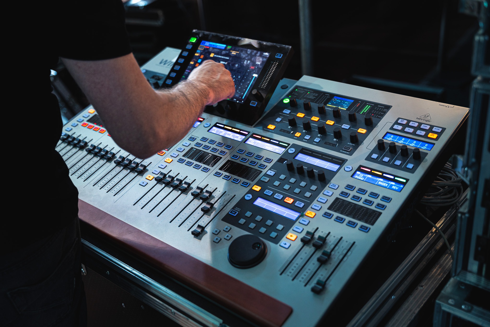 Dłoń osoby obsługującej cyfrowy mikser dźwięku marki Behringer z ekranem dotykowym i suwakami podczas wydarzenia na żywo, widok z bliska.