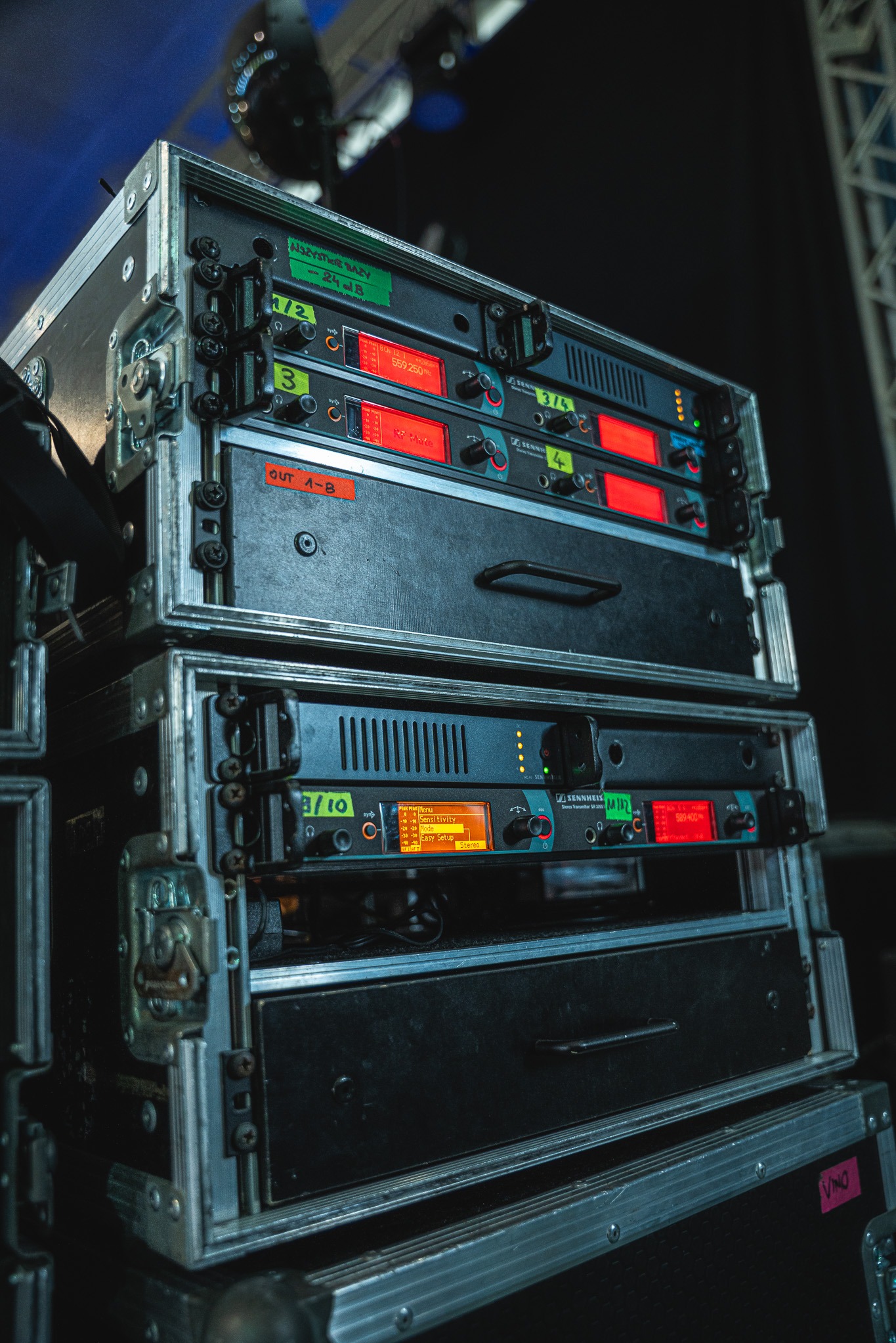 Sprzęt nagłośnieniowy Sennheiser w skrzyniach transportowych, z widocznymi wyświetlaczami i oznaczeniami kanałów, gotowy do użycia na imprezie.