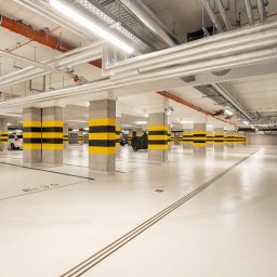 GB Foods Grzegorz Bandzarewicz - Nowoczesny garaż podziemny z oznaczonymi miejscami parkingowymi, kolumny w pasy żółto-czarne, sufit z instalacjami. Czysta, jasna przestrzeń.