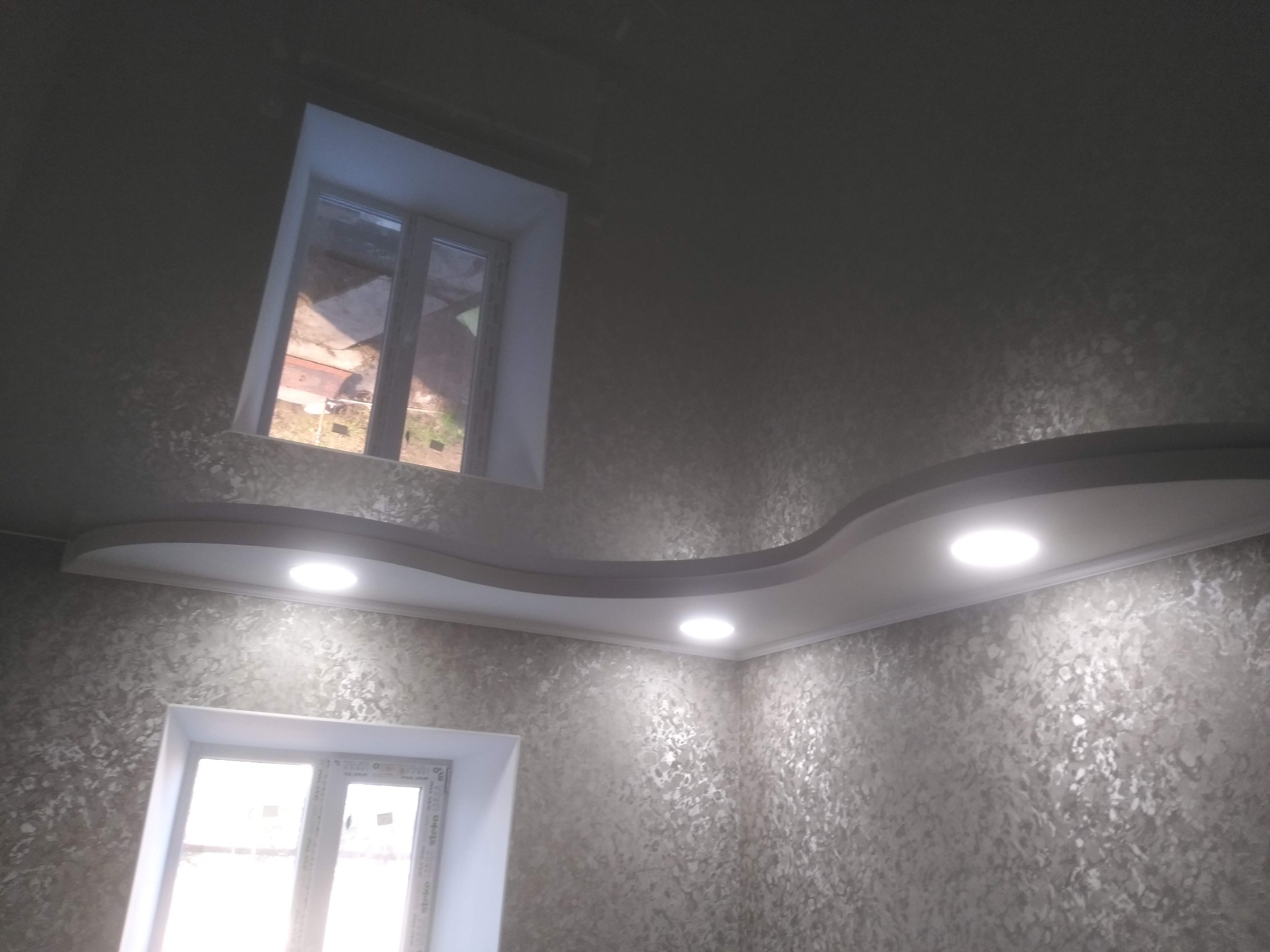 Dekoracyjna ściana z efektem strukturalnym i podwieszany sufit z oświetleniem punktowym. Dwa okna w białych ramach.