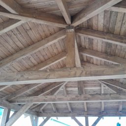 Usługi Dekarskie Piotr Zaremba - Drewniana konstrukcja dachu od wewnątrz, widoczne belki i deski w jasnym odcieniu brązu, tworzące geometryczny wzór. Solidne wykonanie, perspektywa z dołu.