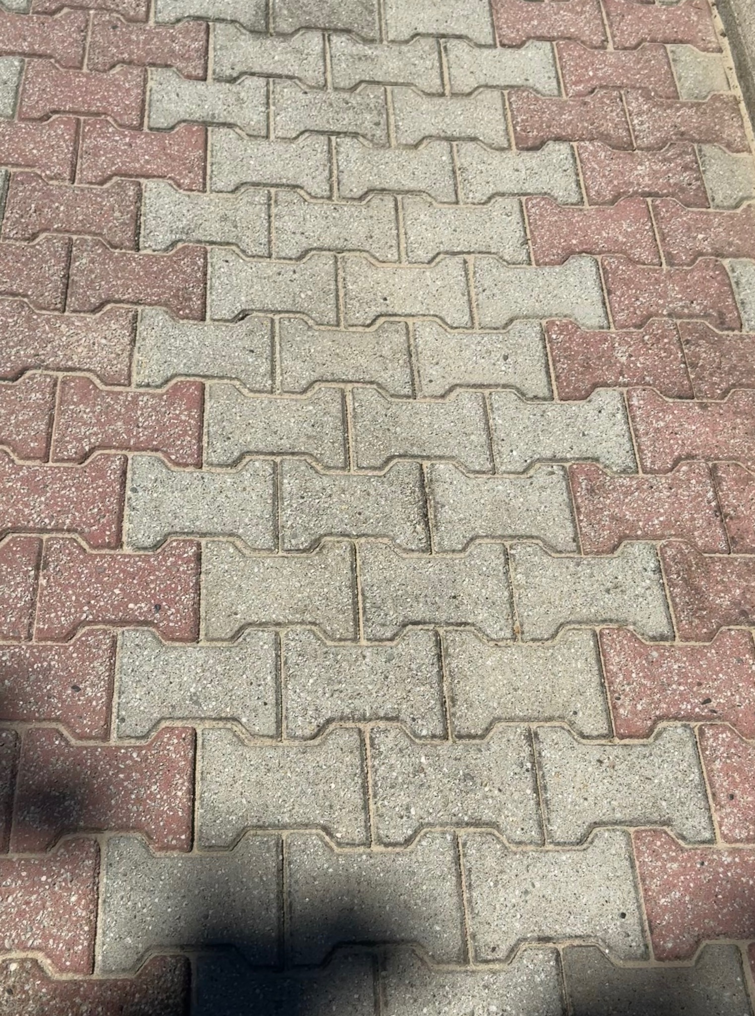 Ułożona kostka brukowa w odcieniach szarości i czerwieni, wzór jodełki, widok z góry, lekki cień w dolnej części kadru.