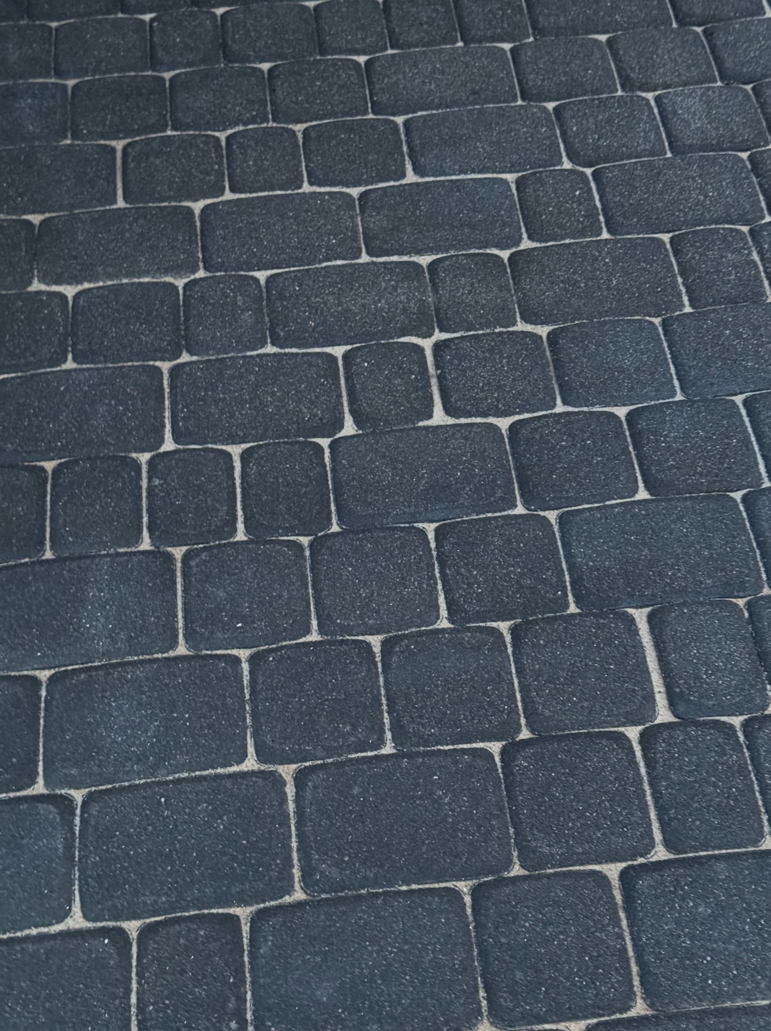Ciemnoszara kostka brukowa ułożona w regularny wzór, widok z góry pod kątem. Jasne fugi kontrastują z ciemnym kolorem kostki.