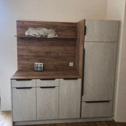 Mateusz Stronczek - Jasna zabudowa kuchenna z drewnianym blatem i półką, widoczna z boku, z elementami dekoracyjnymi na blacie i półce. Uwagę zwraca faktura frontów szafek.