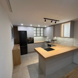 Mateusz Stronczek - Nowoczesna kuchnia z szarymi szafkami i drewnianym blatem. Czarne akcenty oświetleniowe i sprzęt AGD. Jasne płytki podłogowe. Minimalistyczny design.