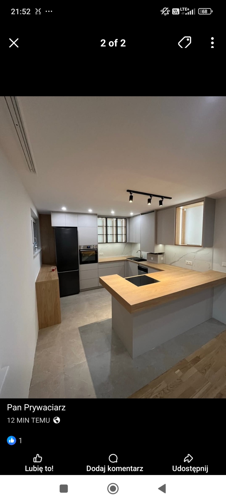 Nowoczesna kuchnia z szarymi szafkami i drewnianym blatem. Czarne akcenty oświetleniowe i sprzęt AGD. Jasne płytki podłogowe. Minimalistyczny design.