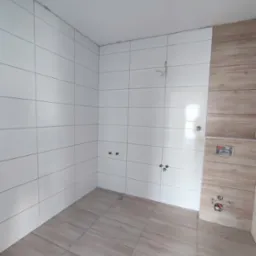 Białe i drewnopodobne płytki w łazience, widoczne przyłącza wodne, efekt po pracach glazurniczych, jasne wnętrze, płytki podłogowe w odcieniach beżu.