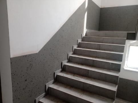 Klatka schodowa z szarymi schodami i ścianami pomalowanymi do połowy na szaro w kropki, oświetlona naturalnym światłem z okna.