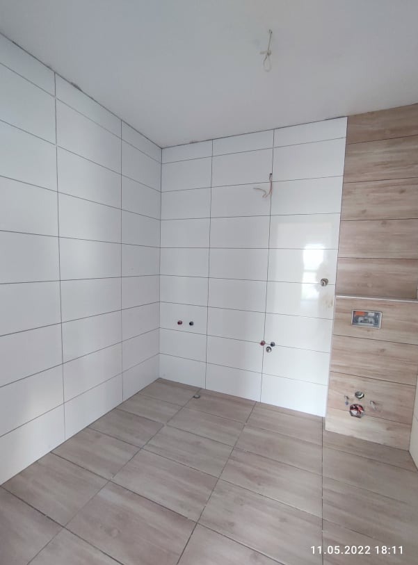 Białe i drewnopodobne płytki w łazience, widoczne przyłącza wodne, efekt po pracach glazurniczych, jasne wnętrze, płytki podłogowe w odcieniach beżu.