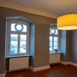 Wnętrze po malowaniu w Morągu: szare ściany, drewniana podłoga, okna z dekoracyjnym szprosowaniem i wisząca lampa. Na parapecie puszka farby.