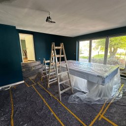 Remontowy Armagedon - Pokój po malowaniu ścian na ciemny turkus, zabezpieczone meble i podłoga, widoczne drabiny malarskie. Widok na ogród przez okno.