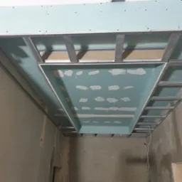 Sufit podwieszany z płyt gipsowo-kartonowych na metalowym stelażu, w trakcie montażu, widok z dołu. Widoczne szpachlowanie łączeń płyt.