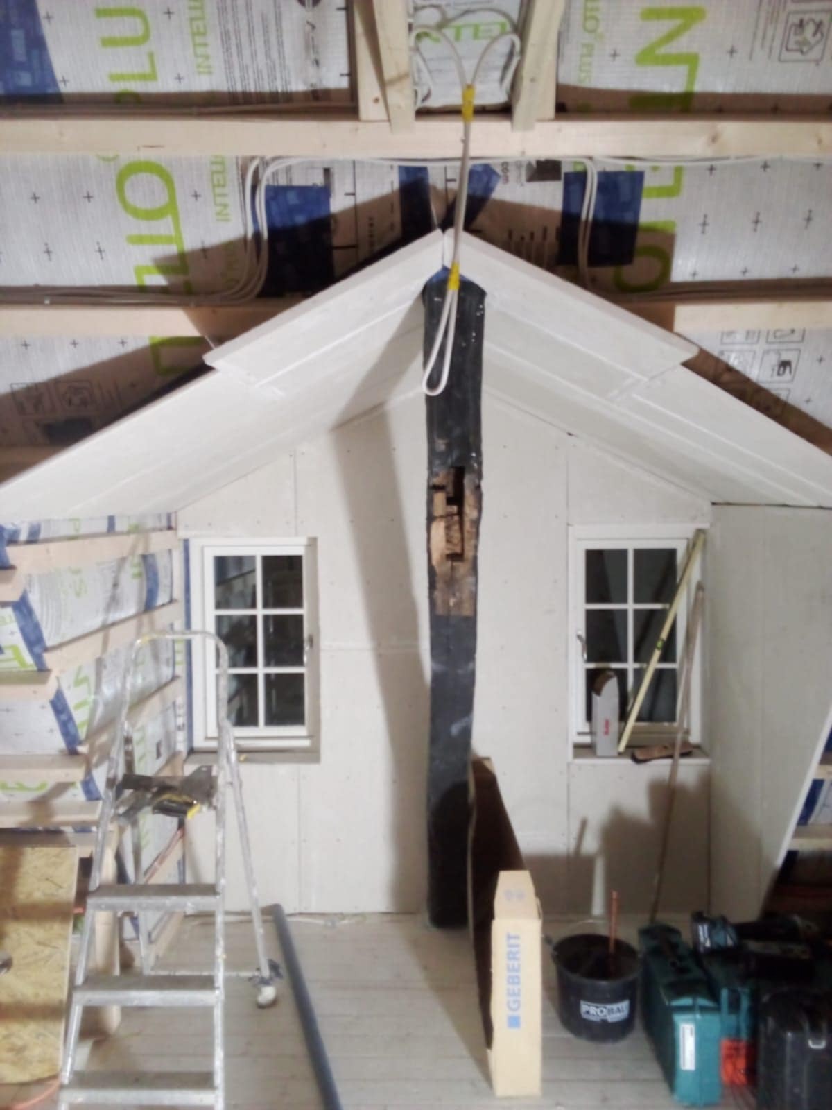 Montaż płyt G-K na poddaszu: widoczne płyty na ścianach, okna, elementy konstrukcyjne dachu, narzędzia. Prace wykończeniowe w trakcie realizacji.