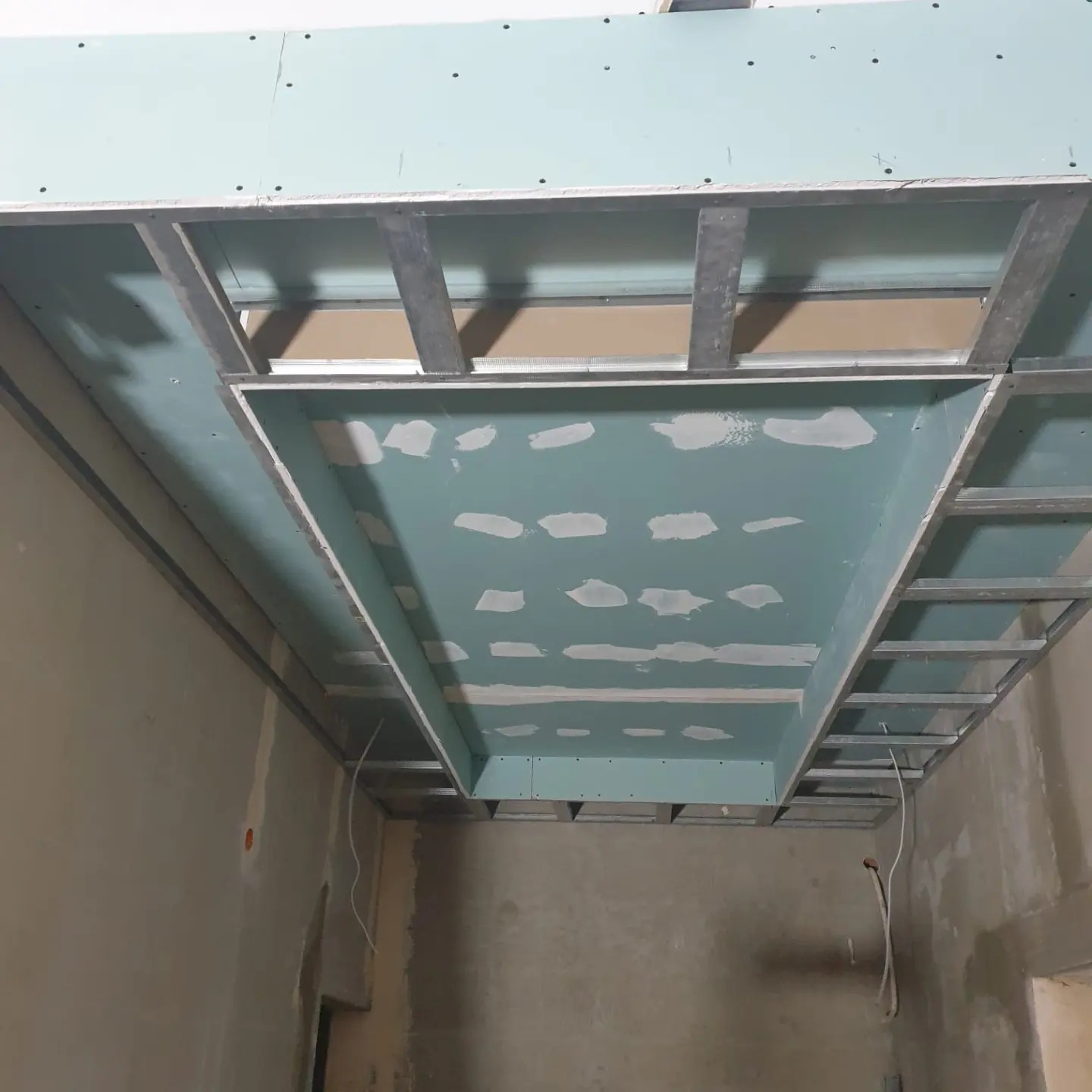 Sufit podwieszany z płyt gipsowo-kartonowych na metalowym stelażu, w trakcie montażu, widok z dołu. Widoczne szpachlowanie łączeń płyt.