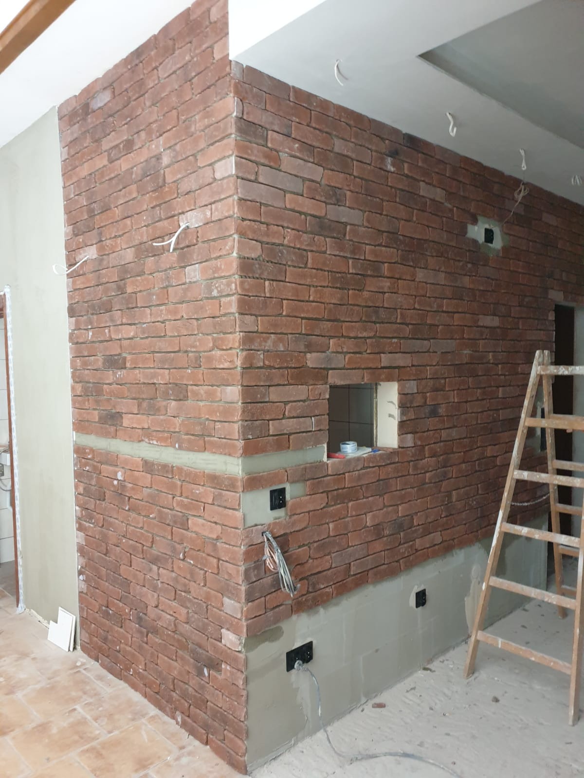 Ściana z cegły klinkierowej w Morągu, z widocznymi puszkami elektrycznymi i fragmentem drabiny. Dekoracyjne wykończenie wnętrza w trakcie realizacji.