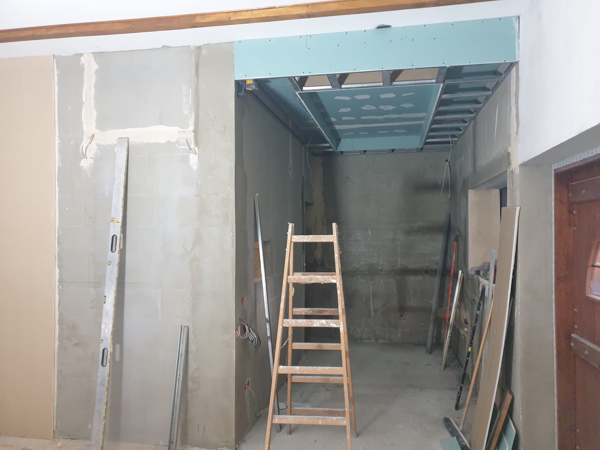 Wnętrze w trakcie prac: ściany po szpachlowaniu, częściowo zamontowana płyta karton-gips na suficie, drabina i poziomica. Widoczne przewody elektryczne.