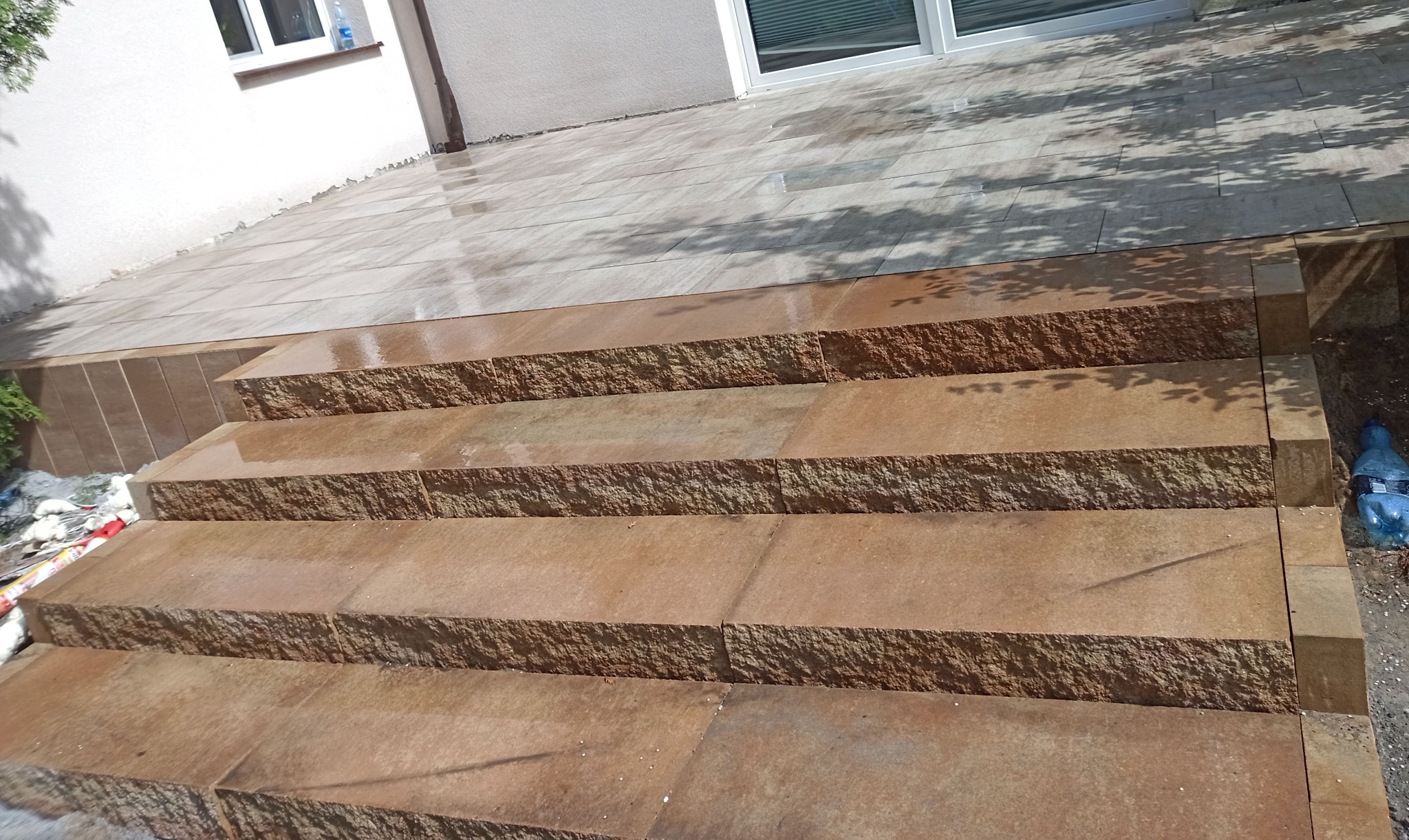 Schody z kostki granitowej prowadzące do domu, z widocznym wykończonym tarasem z płytek. Ciekawa faktura kostki i staranne wykonanie.