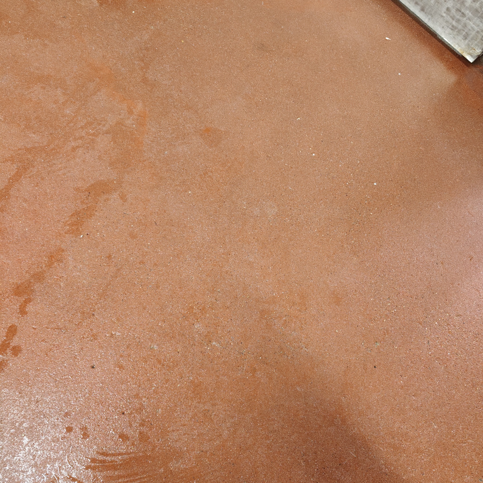 Brudna, terakotowa kostka brukowa z plamami i zaciekami, widoczne ślady po czyszczeniu. Fragment kostki w prawym górnym rogu kadru.