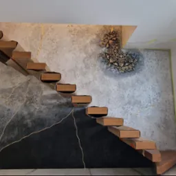 Nowoczesne schody z drewnianymi stopniami na tle ściany z efektem betonu i złotymi żyłkami, zdobione czarnym trójkątem i ornamentem. Widok na okno i wnętrze domu.
