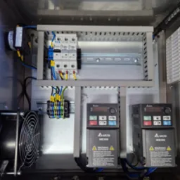 Wnętrze szafy sterowniczej z zamontowanymi elementami elektrycznymi: bezpieczniki EATON, sterowniki Delta ME300, wentylator. Estetyczne ułożenie przewodów.