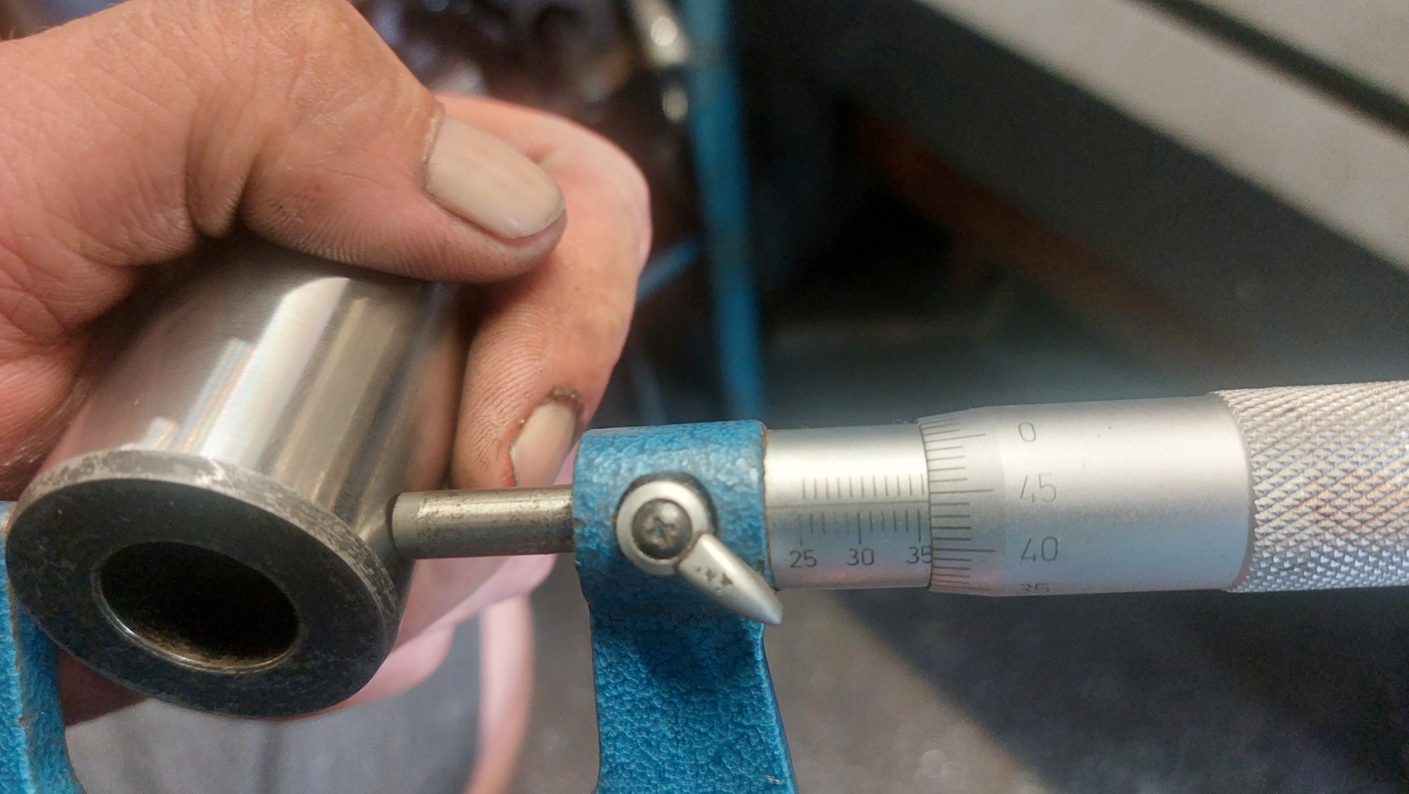 Pomiar suwmiarką wewnętrznej średnicy metalowego elementu. Widoczne drobne zabrudzenia na dłoni i narzędziu, co sugeruje użycie w warsztacie.