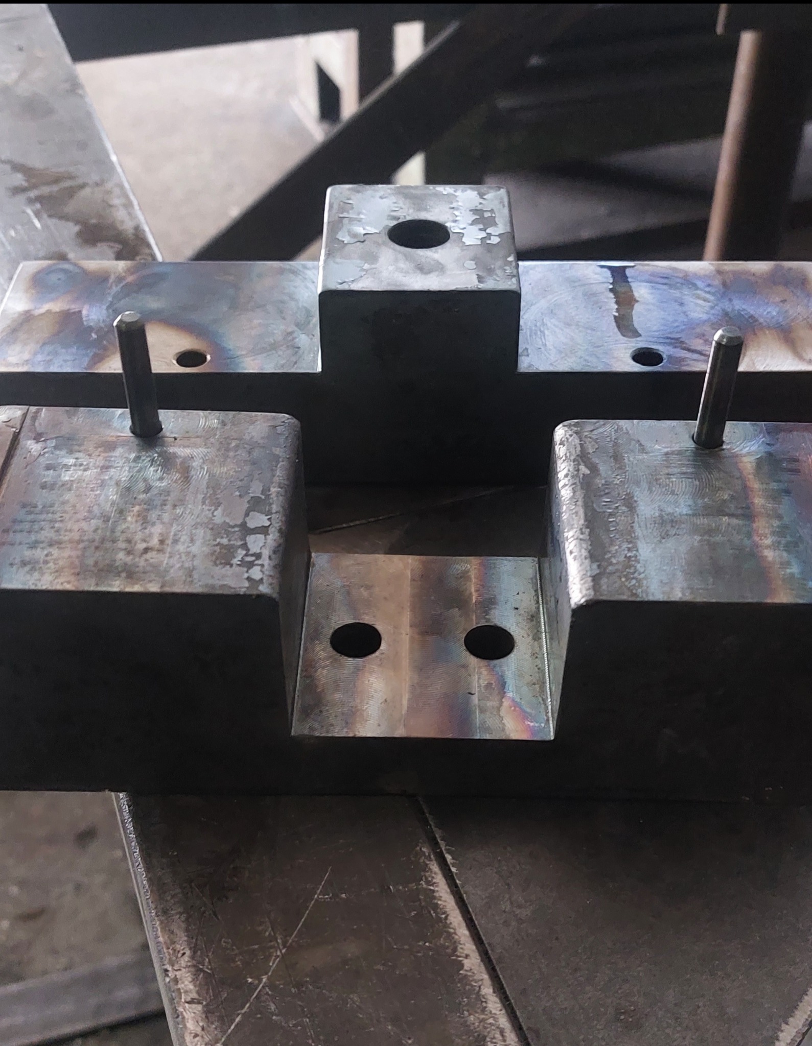 Metalowy element konstrukcyjny z otworami i pinami, przypominający formę odlewniczą. Widoczne ślady obróbki i przebarwienia termiczne na powierzchni.