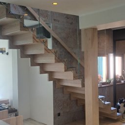 Krzysztof Łosiński Producent Schodów - Nowoczesne schody z jasnego drewna i szklanymi balustradami w jasnym wnętrzu. Widoczny fragment blatu z narzędziami i pies.