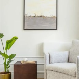 Holy Moly Terapie Anna Bielańska - Jasny pokój z abstrakcyjnym obrazem w czarnej ramie nad fotelem. Na stoliku obok stoi roślina doniczkowa i filiżanka na książce. Minimalistyczny wystrój wnętrza.