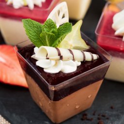 CENTRAL FUND OF IMMOVABLES SPÓŁKA Z OGRANICZONĄ ODPOWIEDZIALNOŚCIĄ - Deser czekoladowy w przezroczystym kubeczku, udekorowany bitą śmietaną, miętą i karambolą, na czarnym kamieniu. W tle inne desery.