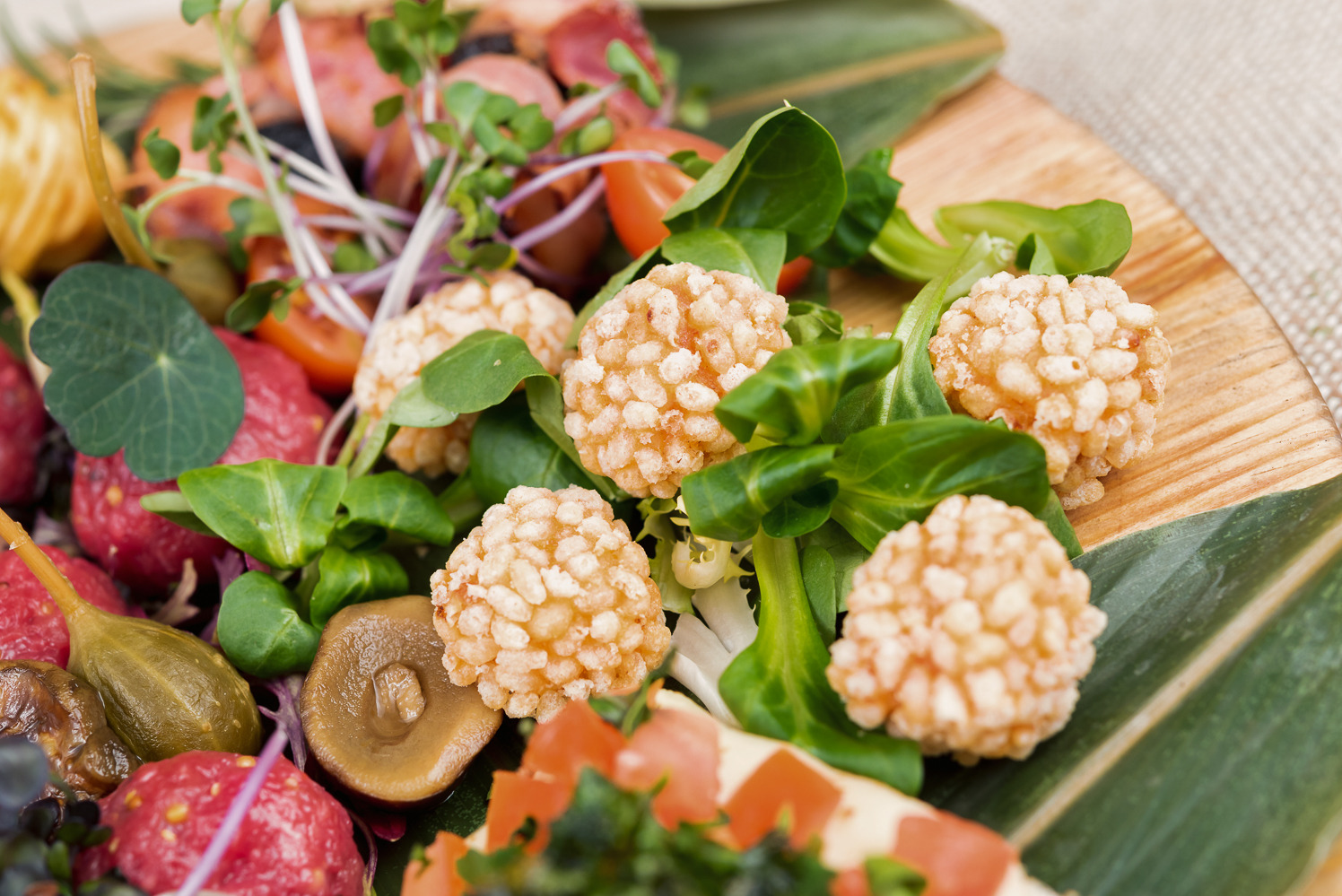 Dekoracyjna kompozycja kulinarna na drewnianej desce: kulki z ryżu, świeże warzywa, grzyby i kiełki, tworzą apetyczną i artystyczną prezentację.