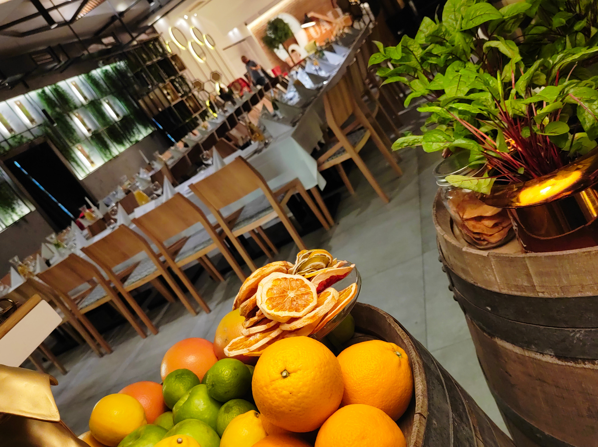 Dekoracja stołu cateringowego z owocami cytrusowymi i suszonymi pomarańczami w rustykalnym stylu, beczka i roślina. W tle nakryty stół.